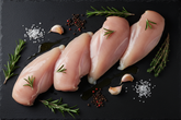 Raw luxury chicken fillet on black slate background with prop ingredients